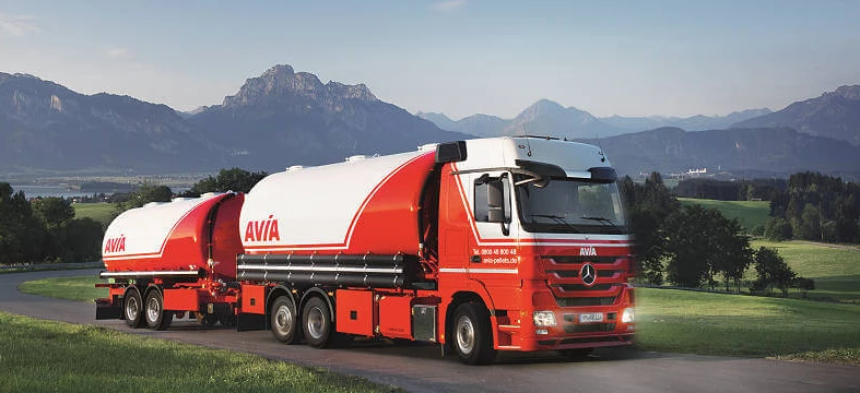 Commercial vehicle with AVÍA logo parked in front of a storage tank. Semi-trailer truck with AVIA branding and Mercedes-Benz features. Ideal for freight transport.