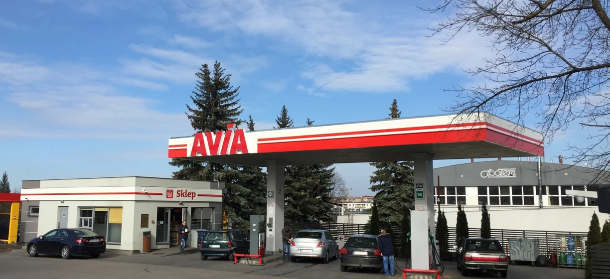 Luxury vehicle parked at fuel station. AVIA Sklep sign in Polish. Family car getting gas.