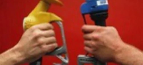 A tradesman in workwear uses a fuel dispenser nozzle to fill a machine with fuel through a pipe and hose.