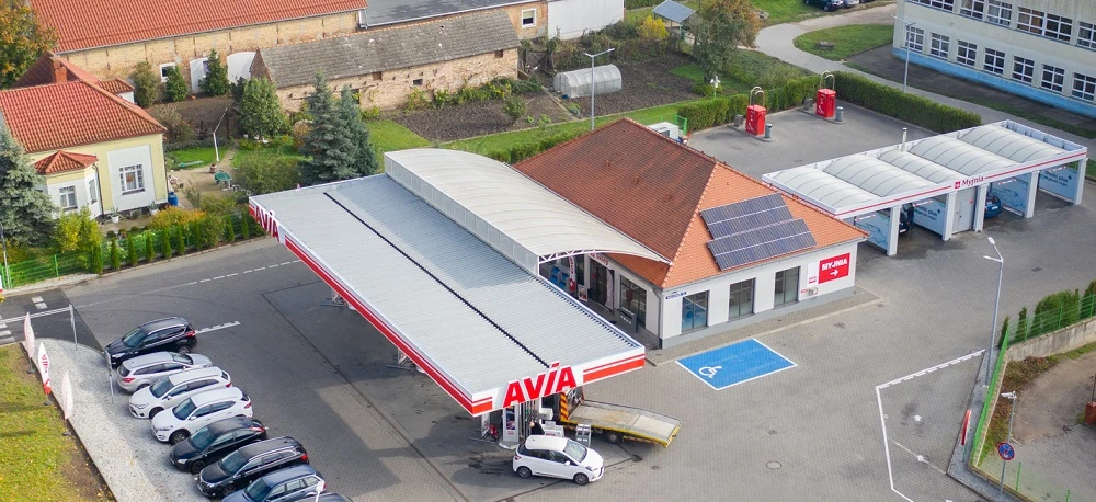 A busy parking lot at a filling station with various vehicles parked. Trucks, SUVs, and subcompact cars fueling up while automotive tail and brake lights illuminate.