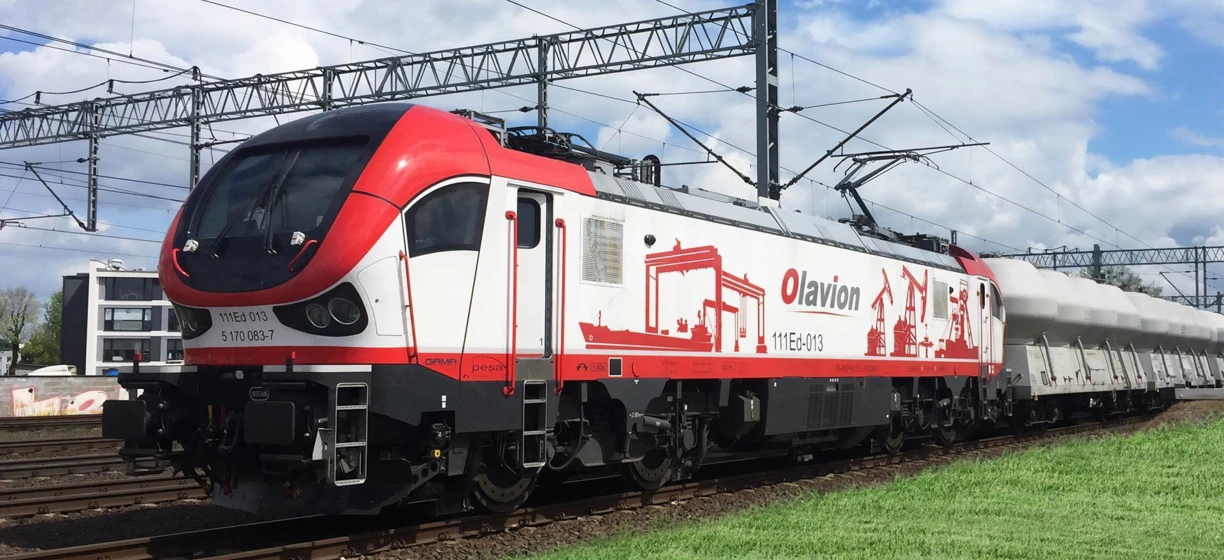 Lokomotywa podróżująca wzdłuż toru kolejowego, część systemu transportu publicznego. Słowa kluczowe obejmują pociąg, transport, tabor, i inżynieria.