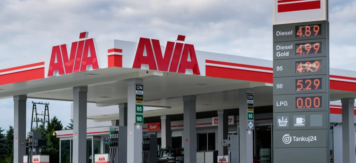 A gas station with fuel prices displayed on digital screens for Diesel, Gold, and LPG. Keywords include AVA, AVIA, FUR, ON, and Tankuj24.