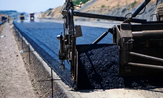 Ciężki sprzęt rozładowuje asfalt na powierzchni drogi, tworząc gładką autostradę. Maszyna układa smołę, beton i żwir, niezbędne materiały budowlane do projektów infrastrukturalnych.